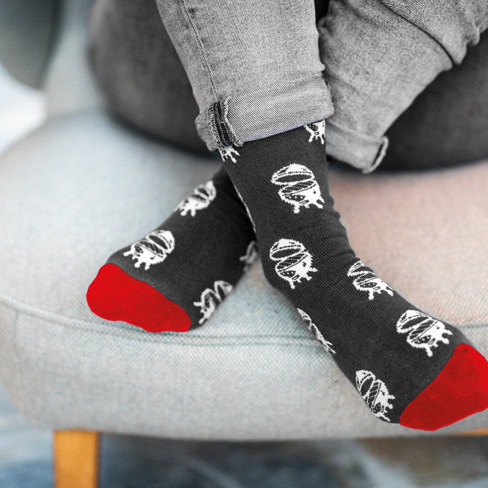 Iemand zit op een lichtblauwe stoffen stoel met de benen opgetrokken en bij de enkels gekruist. De persoon draagt de grijs, rode sokken van Big Green Egg.