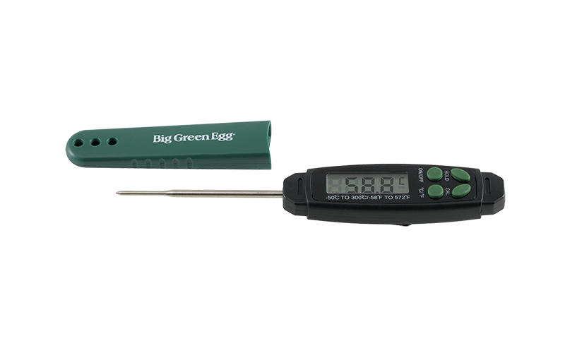 Een digitale thermometer van Big Green Egg. Het apparaat heeft een zwart displaygedeelte met knoppen en een metalen meetpen. Ernaast ligt een groene beschermhoes met het logo "Big Green Egg". De thermometer is ontworpen om snel en nauwkeurig de temperatuur van voedsel te meten, met een meetbereik van -50°C tot 300°C.