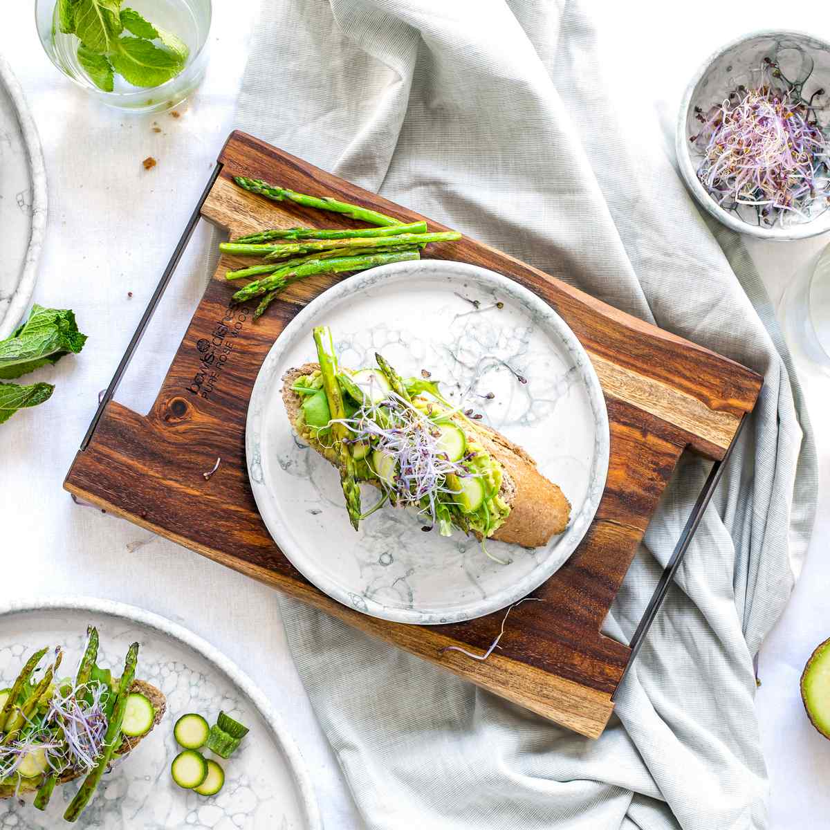 Hetzelfde handgemaakt aardewerken bord in een decoratieve setting op een olijfhouten serveerplank. Op en rond het bord liggen verschillende groenten.