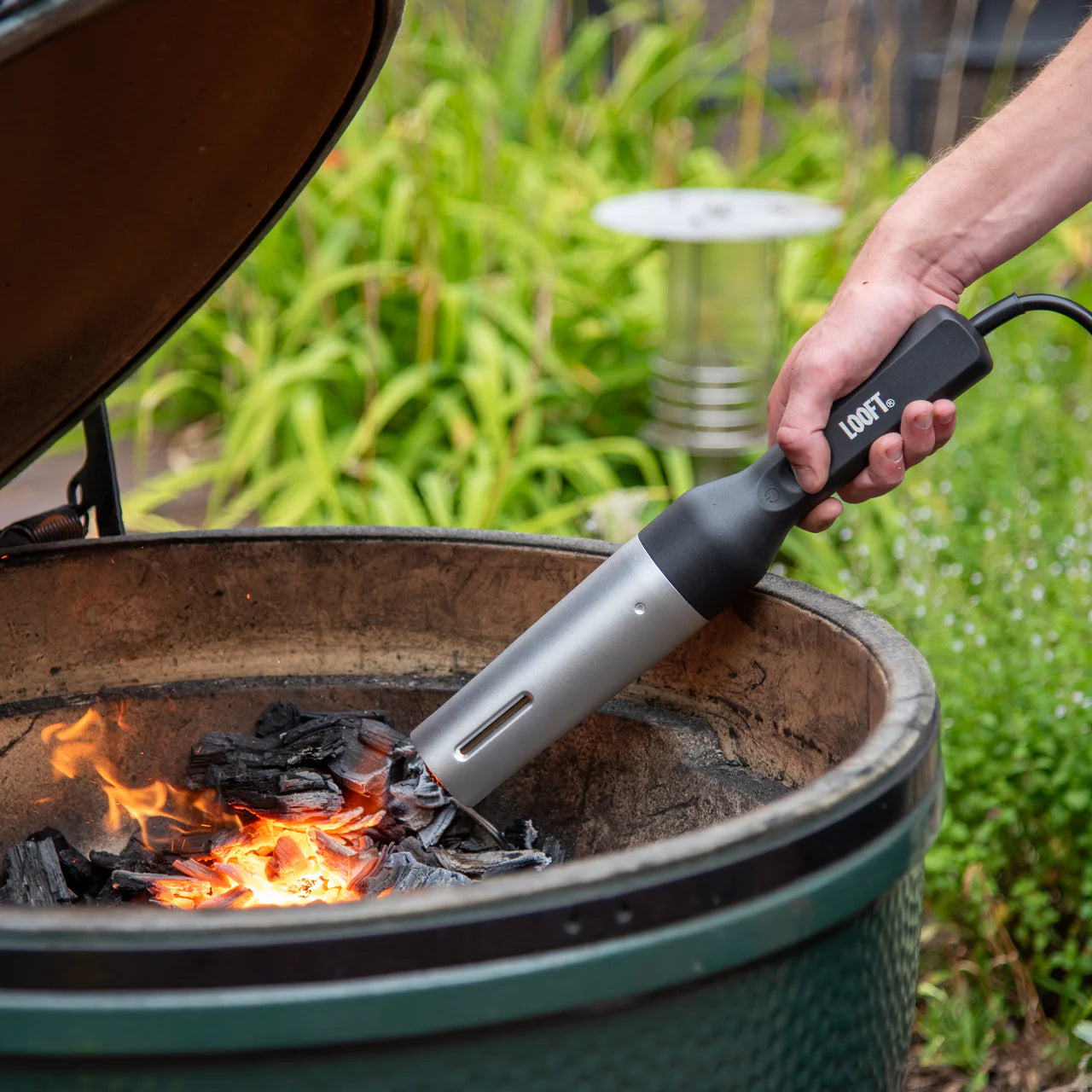 Een man staat buiten en steekt met de Looft Air Lighter het houtskool in de Big Green Egg aan.