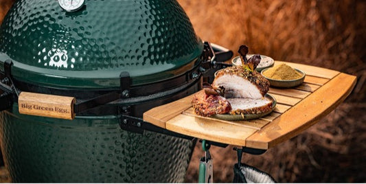 De acacia houten zijtafeltjes bevestigd aan een Big Green Egg. Op het zijtafeltje is een bordje gepaatst met gegrild en gesneden vlees en 2 kommetjes met kruiden.