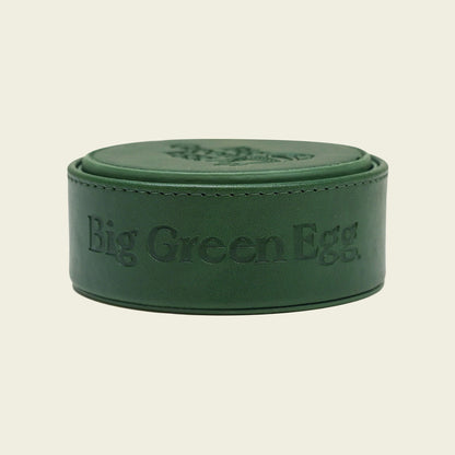De onderzetters met houder vanaf de zijkant in beeld gebracht. De stiknaad aan de bovenkant van de houder wordt hierdoor goed in beeld gebracht, evenals het logo van Big Green Egg dat aan de zijkant in relief is aangebracht.