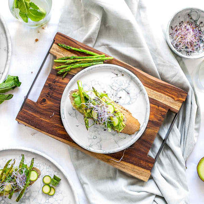 Hetzelfde handgemaakt aardewerken bord in een decoratieve setting op een olijfhouten serveerplank. Op en rond het bord liggen verschillende groenten. 