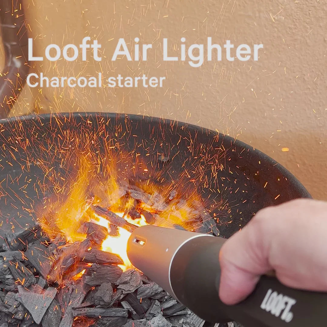 Een man steekt het houtskool in een barbecue aan. In het houtskool is een vuur te zien met fijne vuurvonkjes.