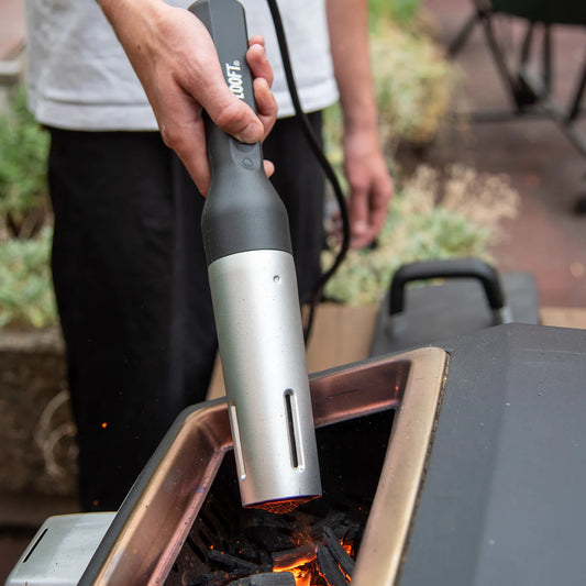 Een man staat buiten en steekt met de Looft Air Lighter de pizza oven aan.