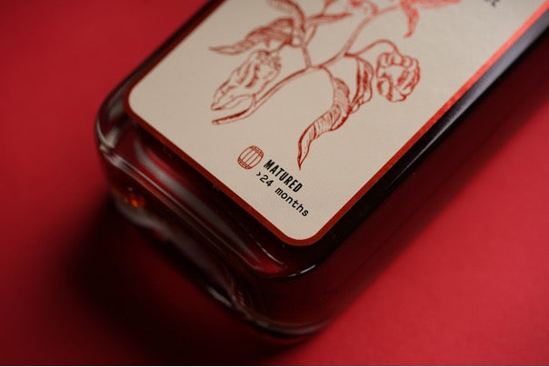 De onderkant van het Tomasu flesje uitgelicht met de tekst "Matured meer dan 24 maanden".